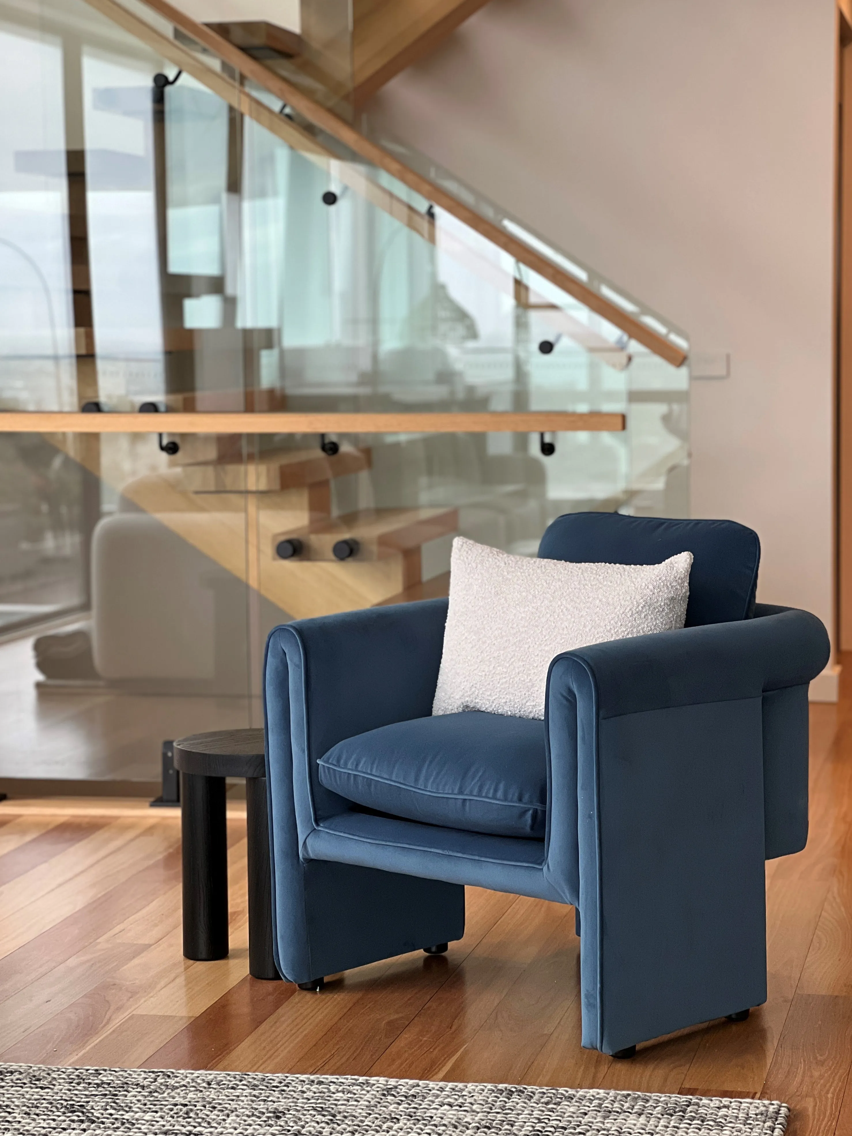 Navy velvet armchair with bouclé cushion beside glass and timber staircase